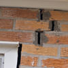 A brick wall displaying stair-step cracks and messy tuckpointing on a New Braunfels home